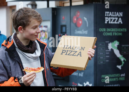 Reischach, Italy, boy proudly shows the box of his pizza pulled out of a machine Stock Photo