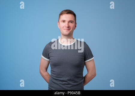 Confident young handsome man keeping arms crossed and smiling while standing against blue white background Stock Photo