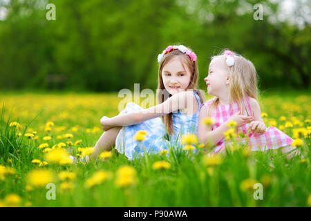 Adorable little girls having fun together in blooming dandelion meadow on beautiful spring day Stock Photo