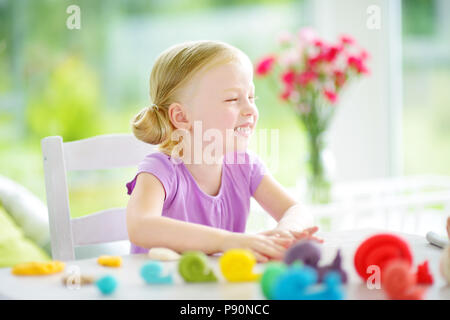 Cute little girl having fun with colorful modeling clay at a daycare. Creative kid molding at home. Child play with plasticine or dough. Stock Photo