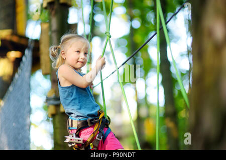 Adorable little girl enjoying her time in climbing adventure park on warm and sunny summer day. Summer activities for young kids. Child having fun on  Stock Photo