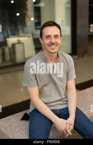 Portrait of smiling man seated on a bench in stone, vertical image Stock Photo