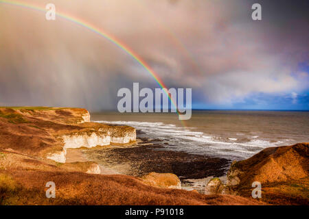 Changeable weather over the limestone cliffs of Flamborough Head, East Yorkshire, England, UK, as an approaching shower of rain brings a rainbow. Stock Photo