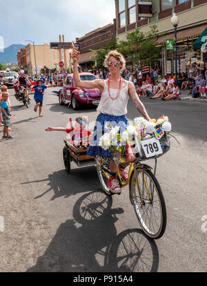 Woman on bicycle pulling son in wagon in annual Fourth of July Parade in the small mountain town of Salida; Colorado; USA Stock Photo