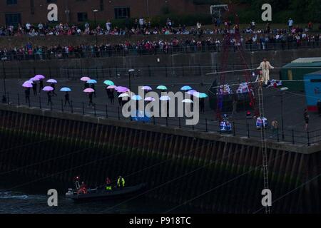 Sunderland, England, 13 July 2018. Performers with illuminated umbrellas dance on the quayside as Chris Bullzini and Johanne Humblet walk across the River Wear from the quayside to Wearmouth Bridge on an inclined high wire, part of Cirque Bijou’s performance “Portolan”. Credit: Colin Edwards/Alamy Live News. Stock Photo