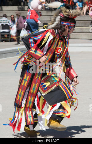 Calgary, Canada. 13th July, 2018.  Young man wearing traditional dress with the addition of a Calgary Flames hockey team logo performs first nations grass dance in Fluor Rope Square, downtown Calgary. The event is part of Calgary Stampede celebrations. Rosanne Tackaberry/Alamy Live News Stock Photo