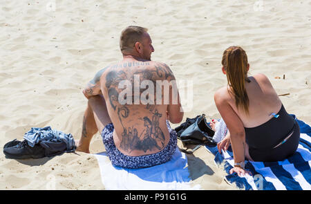 Bournemouth, Dorset, UK. 14th July 2018. UK weather: The heatwave continues with another hot sunny day, as sunseekers make the most of the glorious weather and head to the seaside at Bournemouth beaches. Couple sunbathing, male with tattooed back - tattoos on back. Credit: Carolyn Jenkins/Alamy Live News Stock Photo