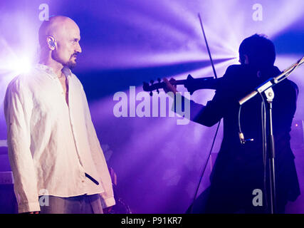 Tim Booth from James performing live at Latitude Festival 2018 and looking at silhouette of band member Saul Davies playing violin, Henham Park, Suffolk, England, 14th July, 2018 Stock Photo