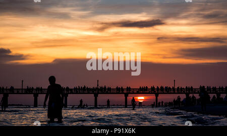 A beautiful sunset behind the Fort Myers Beach Pier as it silhouettes people on the beach. Stock Photo