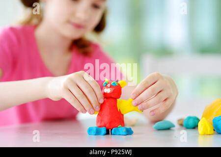 Cute little girl having fun with colorful modeling clay at a daycare. Creative kid molding at home. Child play with plasticine or dough. Stock Photo