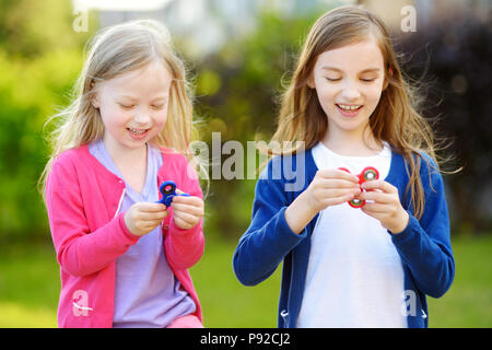 Two funny sisters playing with colorful fidget spinners on the playground. Popular stress-relieving toy for school kids and adults. Stock Photo