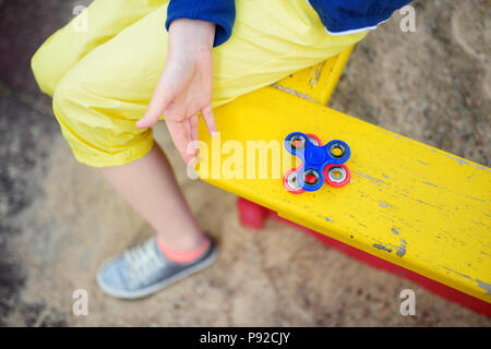 School girl playing with colorful fidget spinner on the playground. Popular stress-relieving toy for school kids and adults. Stock Photo