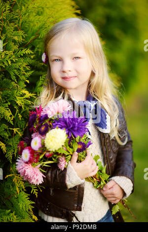 Cute little girl holding colorful aster flowers on beautiful autumn day at city park Stock Photo