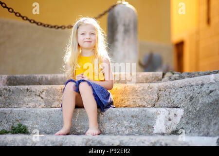 Adorable little girl sitting on the stairs on warm and sunny summer day in Gargnano town in Italy Stock Photo
