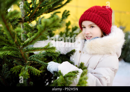 Cute little girl picking a tree at Christmas tree market on chilly winter day. Choosing Xmas tree for family celebration at home. Wonderful Christmas  Stock Photo