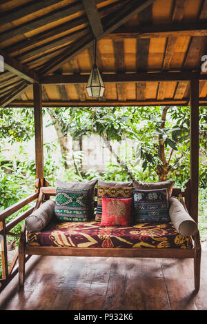 Wooden sofa with pillows on terrace under roof in ethnic style with colorful traditional ornaments Stock Photo