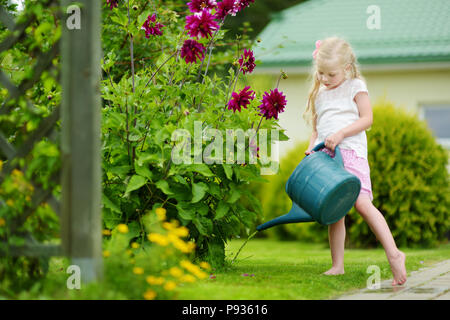 Cute little girl watering flowers in the garden at summer day. Child using garden hose on sunny day. Mommys little helper. Stock Photo