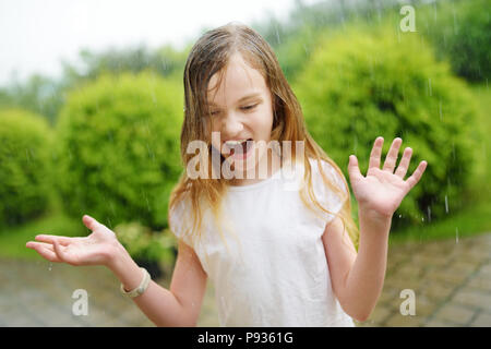 Cute little girl having fun under warm summer rain. Child playing outdoors. Stock Photo