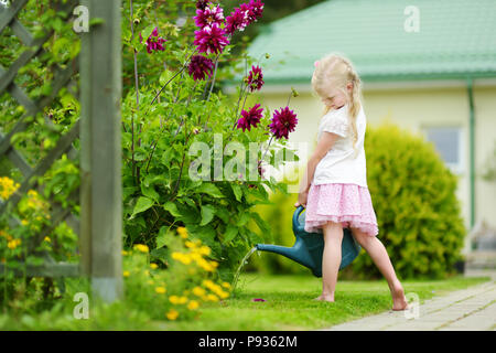 Cute little girl watering flowers in the garden at summer day. Child using garden hose on sunny day. Mommys little helper. Stock Photo