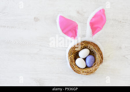 A nest with three colored Easter eggs and bunny ears at home on Easter day. Celebrating Easter at spring. Painting eggs. Stock Photo