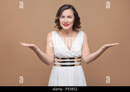 Portrait of angry middle aged boss woman looking at camera. Emotional expressing woman in white dress, red lips and dark curly hairstyle. Studio shot, Stock Photo