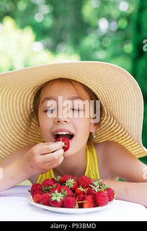 Portrait of Cute teen girl in big hat is eating strawberry at summer day Stock Photo