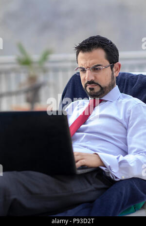 middle aged arab man working during his summer holiday by a pool Stock Photo
