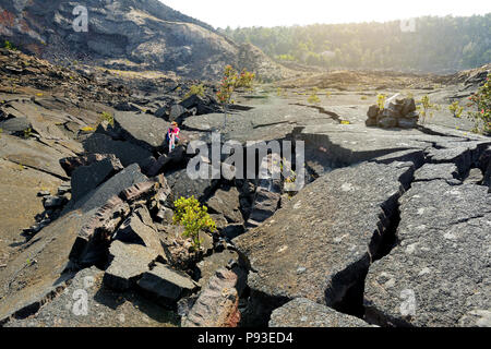 Young female tourist exploring surface of the Kilauea Iki volcano crater with crumbling lava rock in Volcanoes National Park in Big Island of Hawaii,  Stock Photo