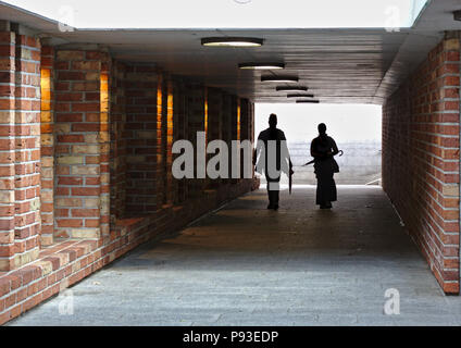 Two people silhouetted against a bright light walking through a tunnel with brick walls towards the camera Stock Photo