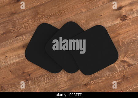 Black square coasters. Isolated on wood background. 3d render Stock Photo