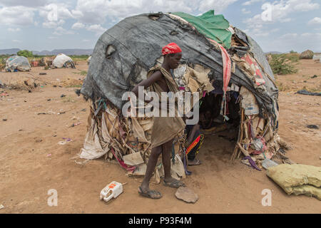 Kakuma, Kenya - On the edge of the refugee camp Kakuma. A young man stands in front of his hut, covered with old plastic tarpaulins, blankets and cardboard boxes. Stock Photo