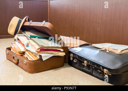 Straw hat is hanging on edge, of old fashioned suitcase made from leather, who is full of folders, papers and documents, overloaded. Stock Photo