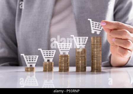 Businesswoman's Hand Placing White Shopping Cart On Top Of Golden Stacked Coins Stock Photo