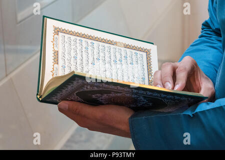 Copy of the holy Quran held by the hands of a man in the white interior of Sultan Qaboos Grand Mosque in Muscat, Oman Stock Photo
