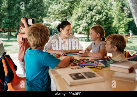 Young students engaged in a class outside in the fresh air. Outdoor learning - school children enjoying a lesson with their teacher. Stock Photo