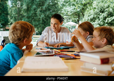 Kids during a reading lesson outside in a park. Teacher reading to children during a school break. Stock Photo
