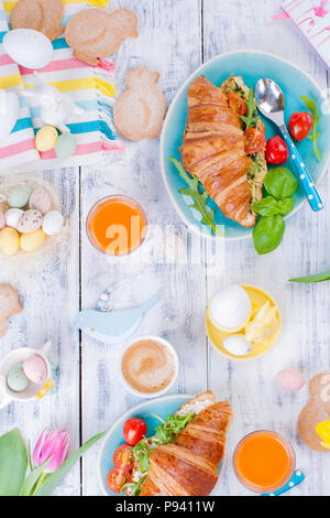 Breakfast for two. Croissants with salad and espresso. Fresh juice and sweets. Spring tulips. Easter decor. White wooden background. Stock Photo