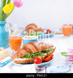 Delicious spring breakfast on a white background. Bouquet of fresh tulips. Small and large colored Easter eggs. Oatmeal, coffee, fresh berries. Stock Photo