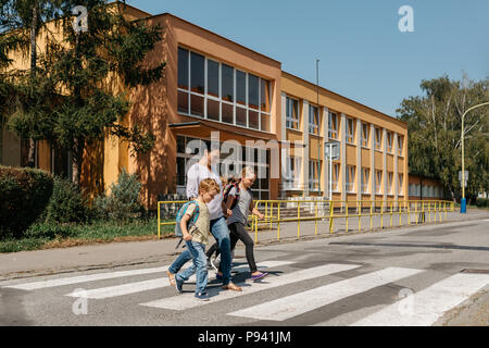 Road safety - children crossing a road accompanied by an adult. Mother picking her children up from school. Stock Photo