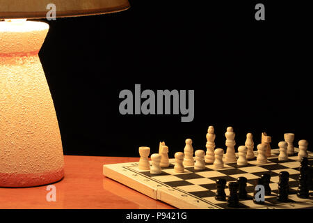 Luminous table lamp standing near chess board on dark background Stock Photo