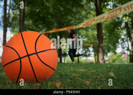 Close-up of an orange traditional eight-panel basketball on the green grass outdoors in the park in a summer day