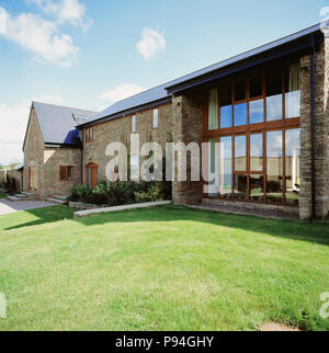 Lawn in front of large windows on modern extension to traditional barn conversion Stock Photo