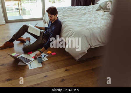 businessman working on laptop computer sitting at home with his diary and official papers. Man making notes in diary and looking at laptop sitting on Stock Photo