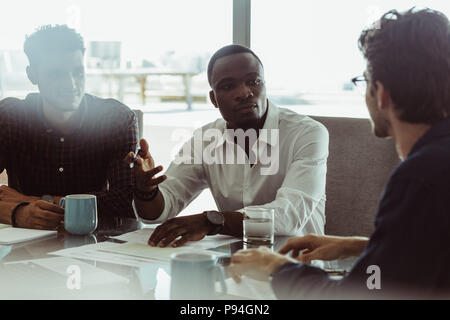 Businessmen discussing work sitting at a conference table in office. Three men in a formal business meeting discussing work. Stock Photo