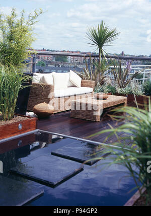 Paving slabs across pool on decked city roof garden with seagrass table and matching sofa with white cushions Stock Photo