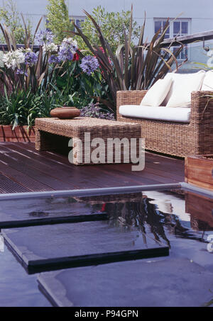Seagrass table and sofa with white cushions on decked roof garden with paving slabs across pool Stock Photo