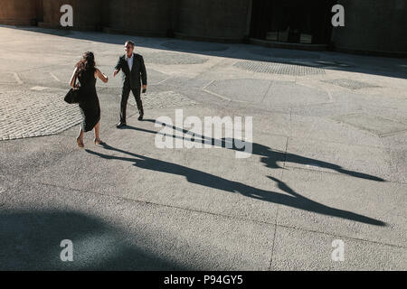 Businesswoman walking forward to shake hands with a colleague outdoors with their long shadows on the ground. Business colleagues greeting each other  Stock Photo