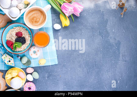 Delicious spring breakfast on a background of gray stone. Bouquet of fresh tulips. Small and large colored Easter eggs. Oatmeal, coffee, fresh berries. Postcard for Easter. Stock Photo