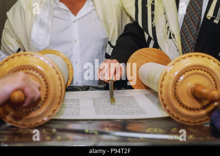 A praying man with a tefillin on his arm and head, holding a Torah scrolls, while reading a pray at a Jewish ritual Bar Mitzvah ceremony . Stock Photo