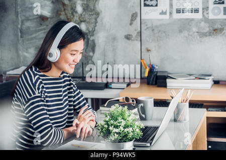 Young asian casual businesswoman arm on desk rest pose with laptop computer and listening music via headphone and think about work ,work at home with  Stock Photo